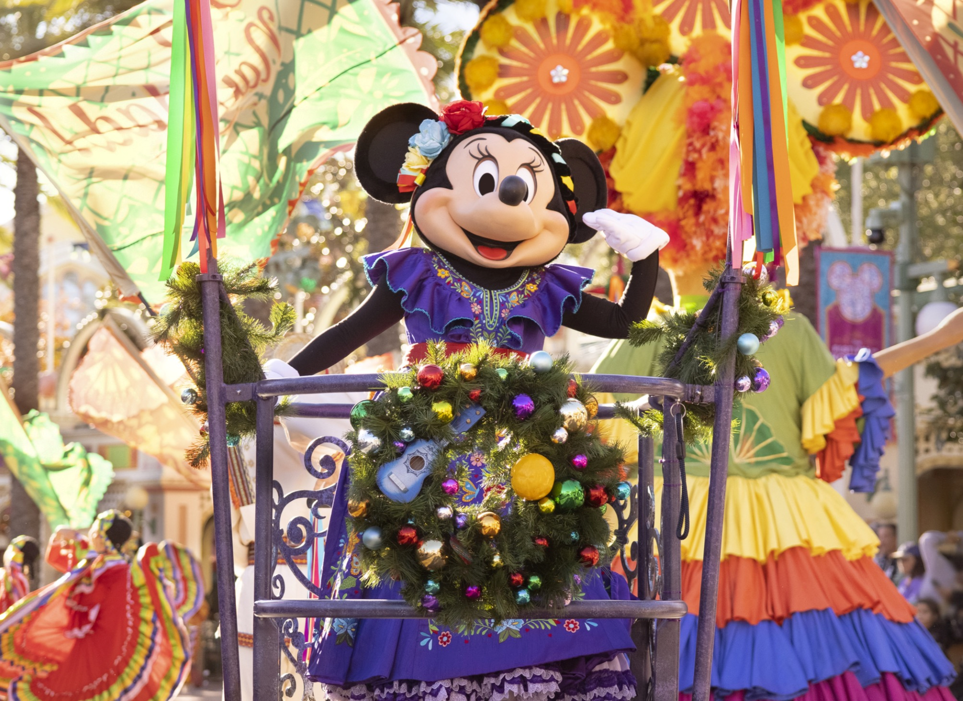 Minnie Mouse in her Disney ¡Viva Navidad! outfit waving from a platform holding a decorated wreath at Disney California Adventure