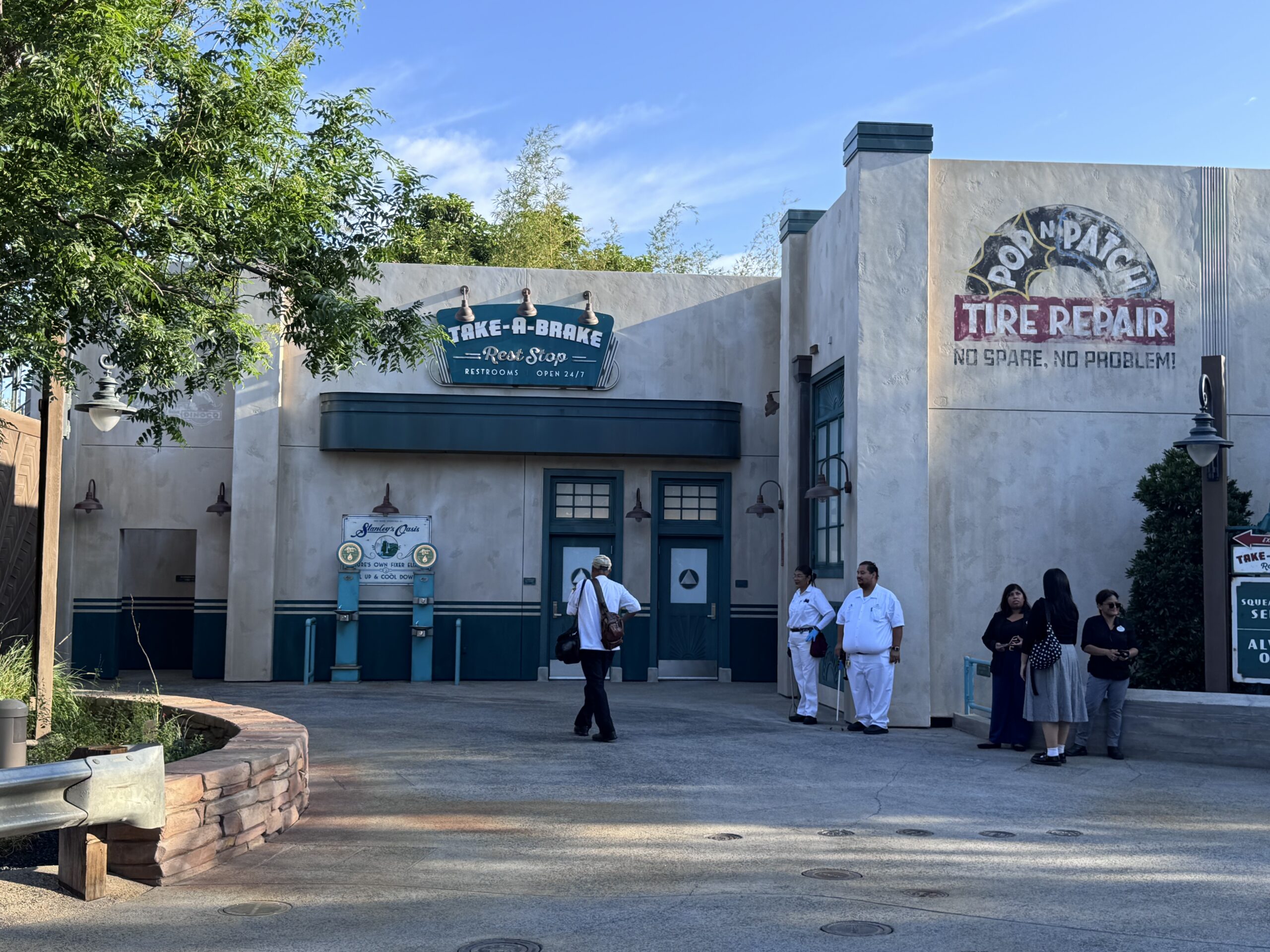 The Take-A-Brake Rest Stop restroom building in Cars Land at Disney California Adventure on its opening day, with the Pop N Patch Tire Repair mural and Stanley's Oasis water fountains