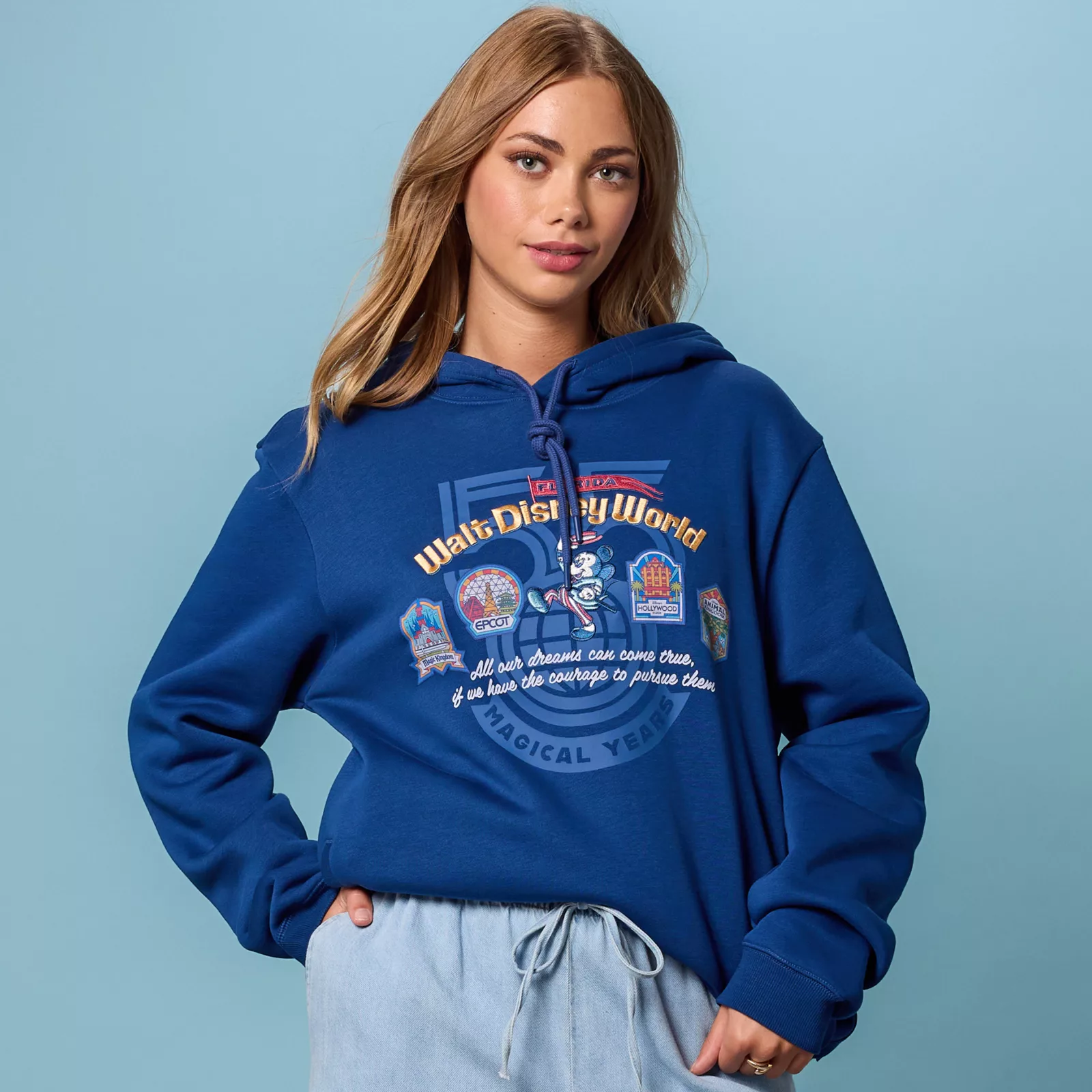 Close-up of the Walt Disney World 55th anniversary hoodie artwork with Mickey marching among the four park badges and the Walt Disney quote