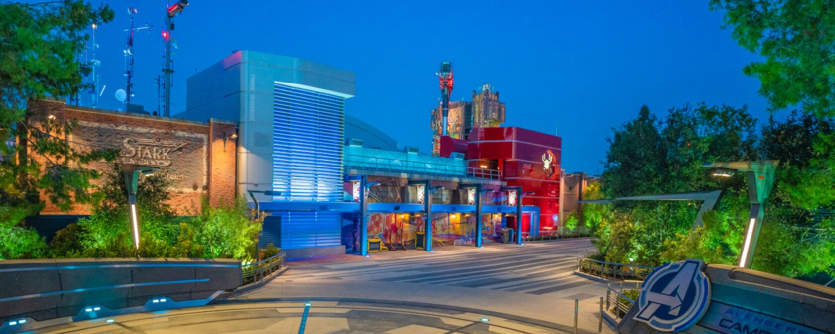 Avengers Campus at dusk, with the Stark sign on the left and the Avengers Campus logo in the foreground