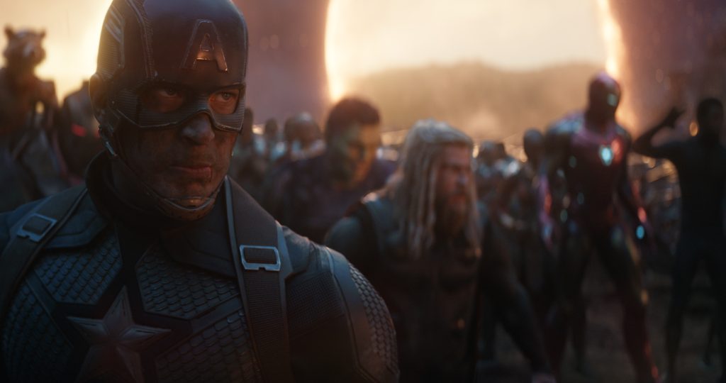 Captain America in his helmet stands in the foreground with Thor, Iron Man, Hulk, Rocket and a crowd of heroes behind him against a glowing portal in a still from Avengers Endgame: Encore (Marvel Studios)