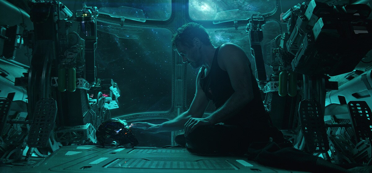 Robert Downey Jr. as Tony Stark sitting on the floor of a spacecraft beside his Iron Man helmet in Avengers: Endgame