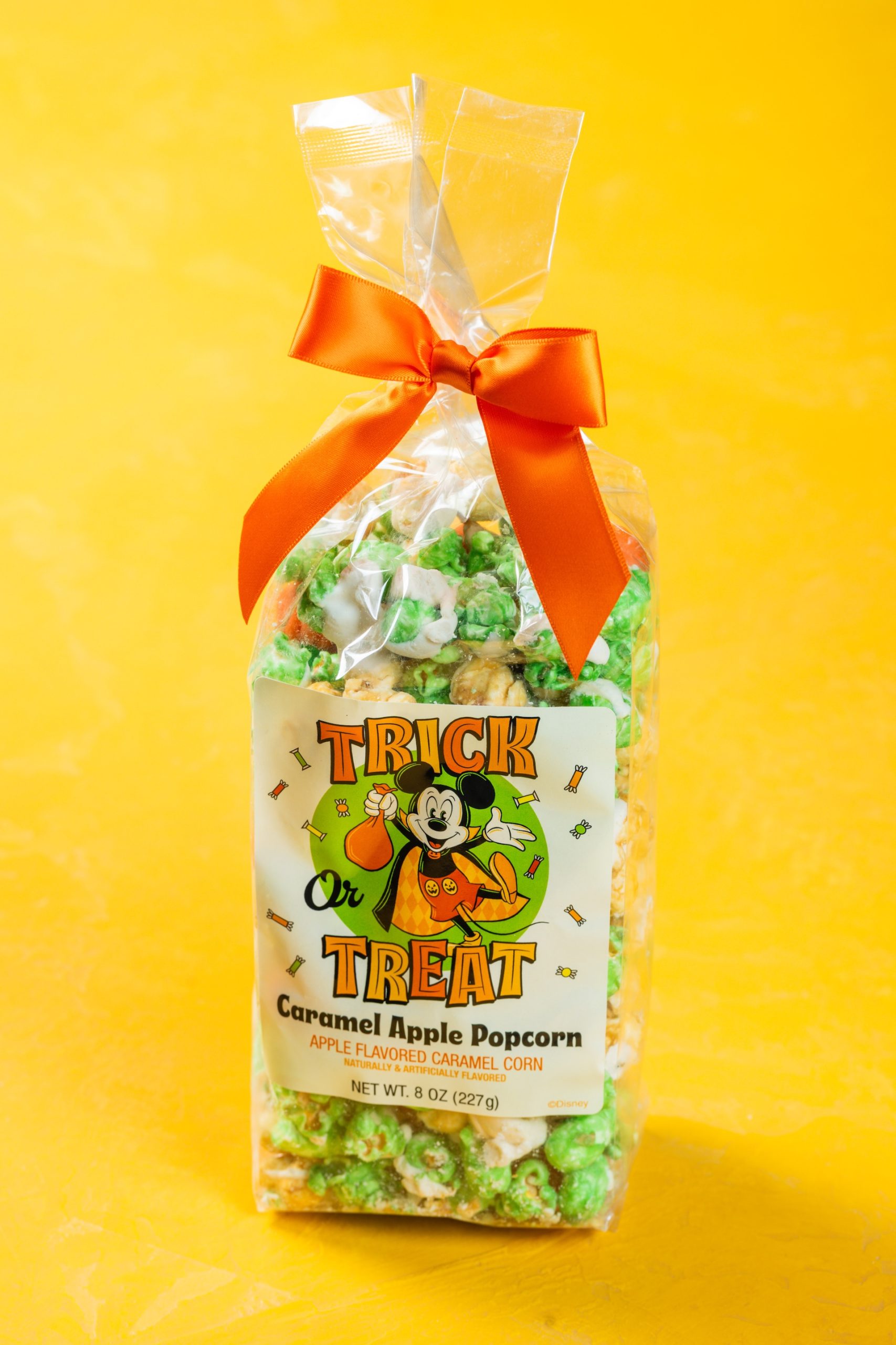 Bag of green Caramel Apple Popcorn tied with an orange bow and a Trick or Treat Mickey Mouse label