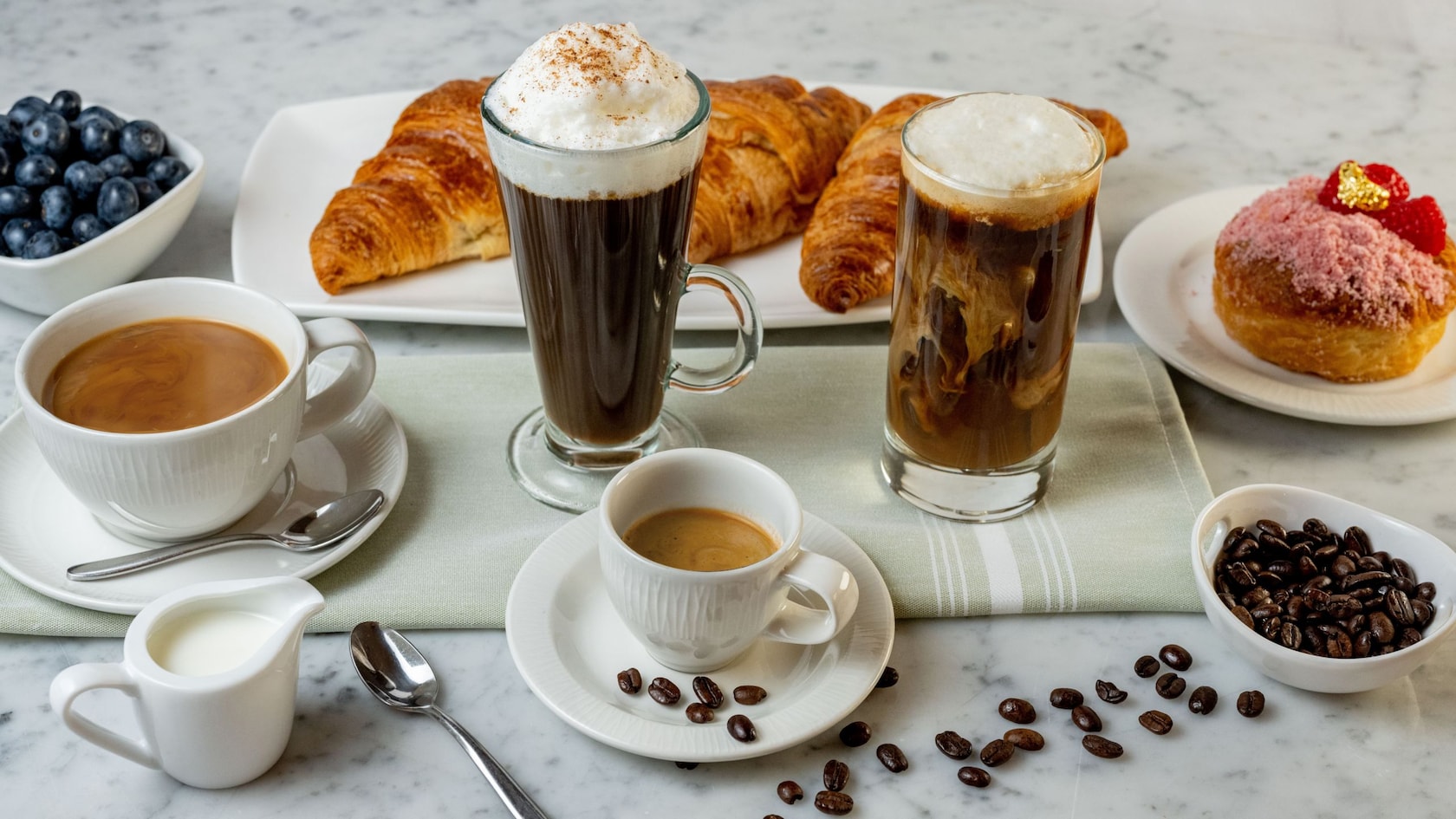 Blueberries, coffee beans, 2 coffee beverages, 2 cups of tea and 2 dishes holding pastries
