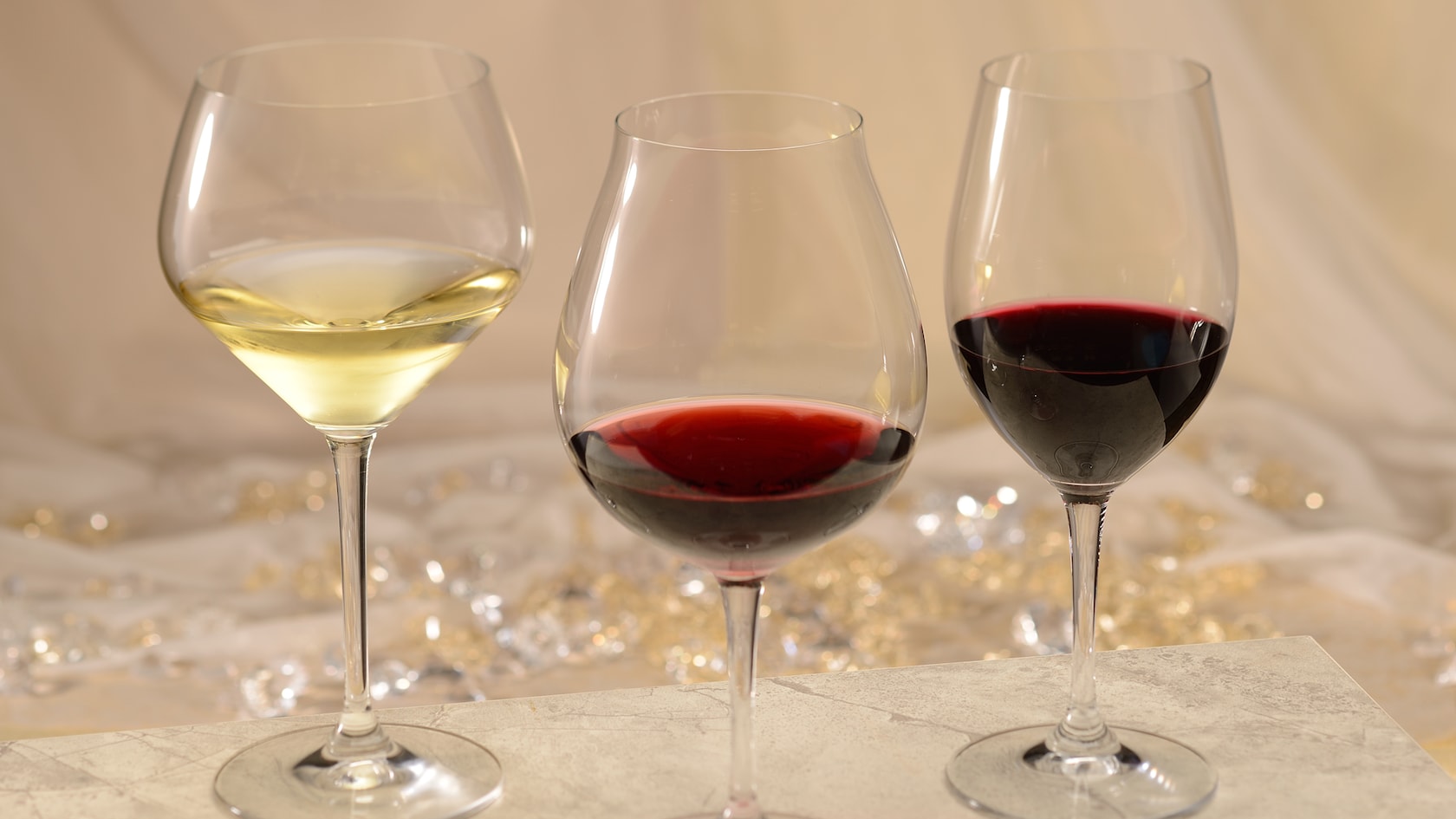 A glass of white wine next to a glass of red wine next to a glass of pinot noir