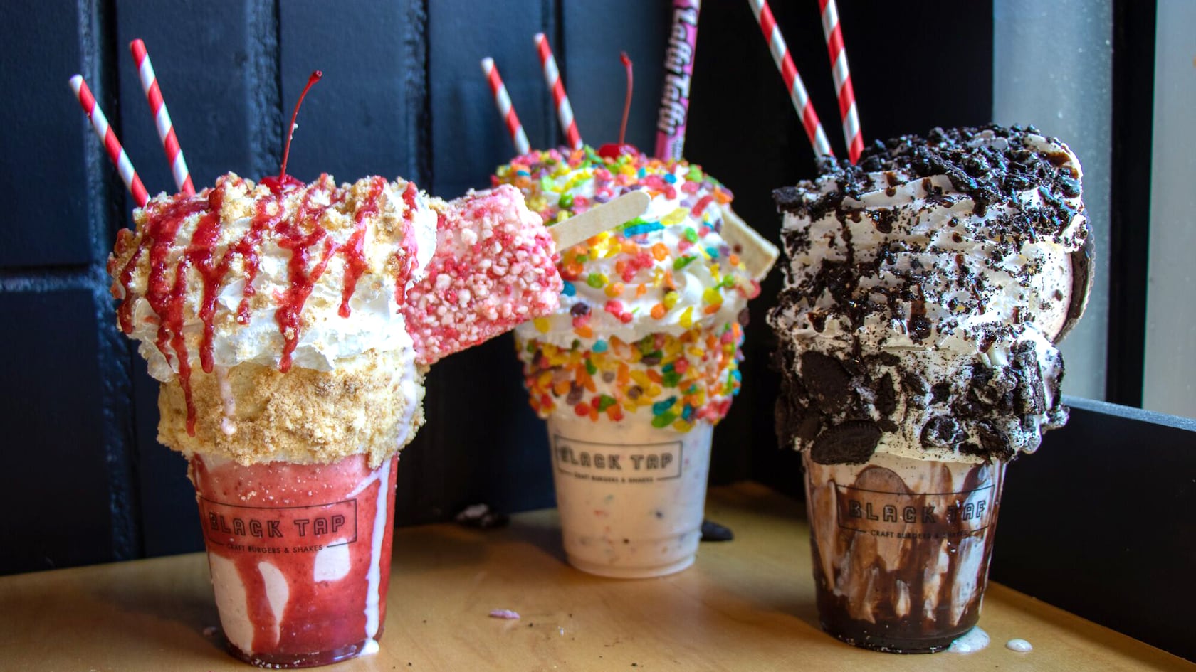 A strawberry milkshake with an ice cream bar, a vanilla milkshake covered in candy and a cookies and cream milkshake
