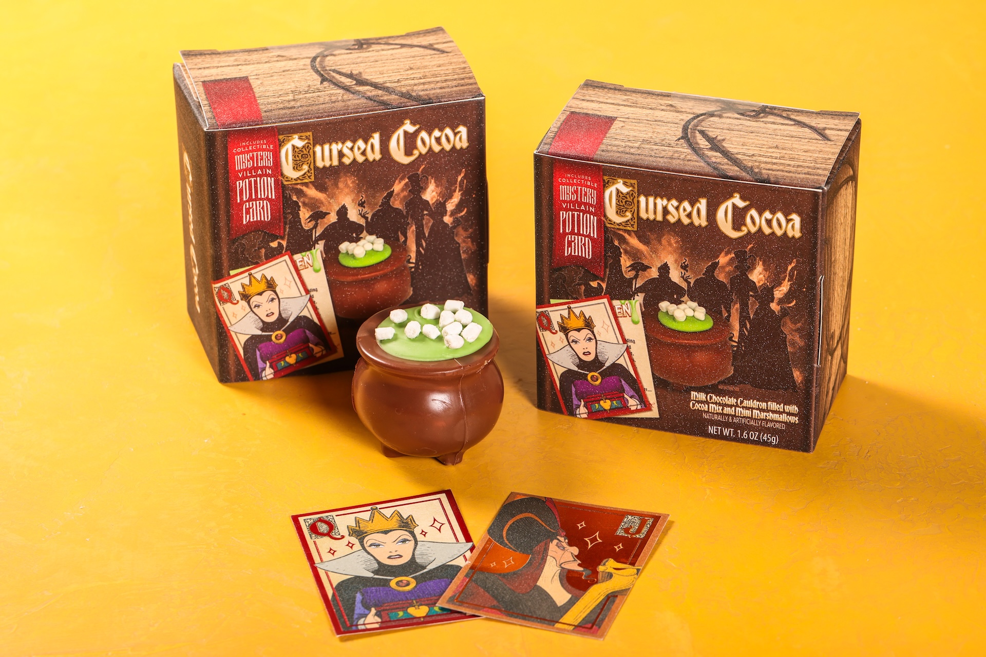 Two Cursed Cocoa boxes and a cauldron of cocoa topped with marshmallows, with potion cards in front