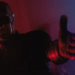 Daredevil in his dark suit and cowl pointing toward the camera under red and blue light in Daredevil: Born Again