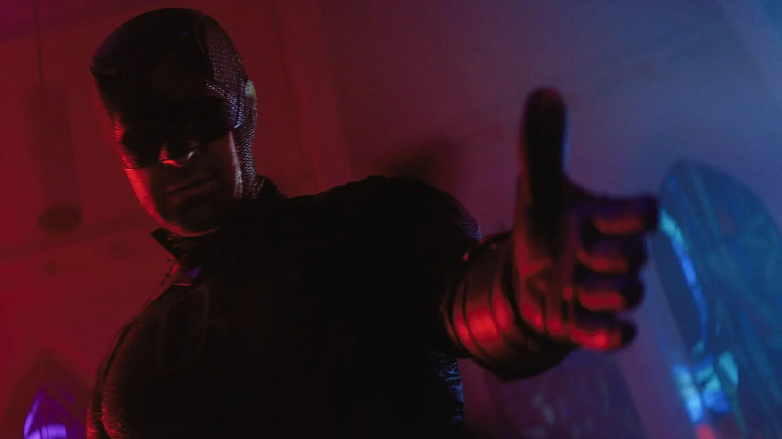 Daredevil in his dark suit and cowl pointing toward the camera under red and blue light in Daredevil: Born Again