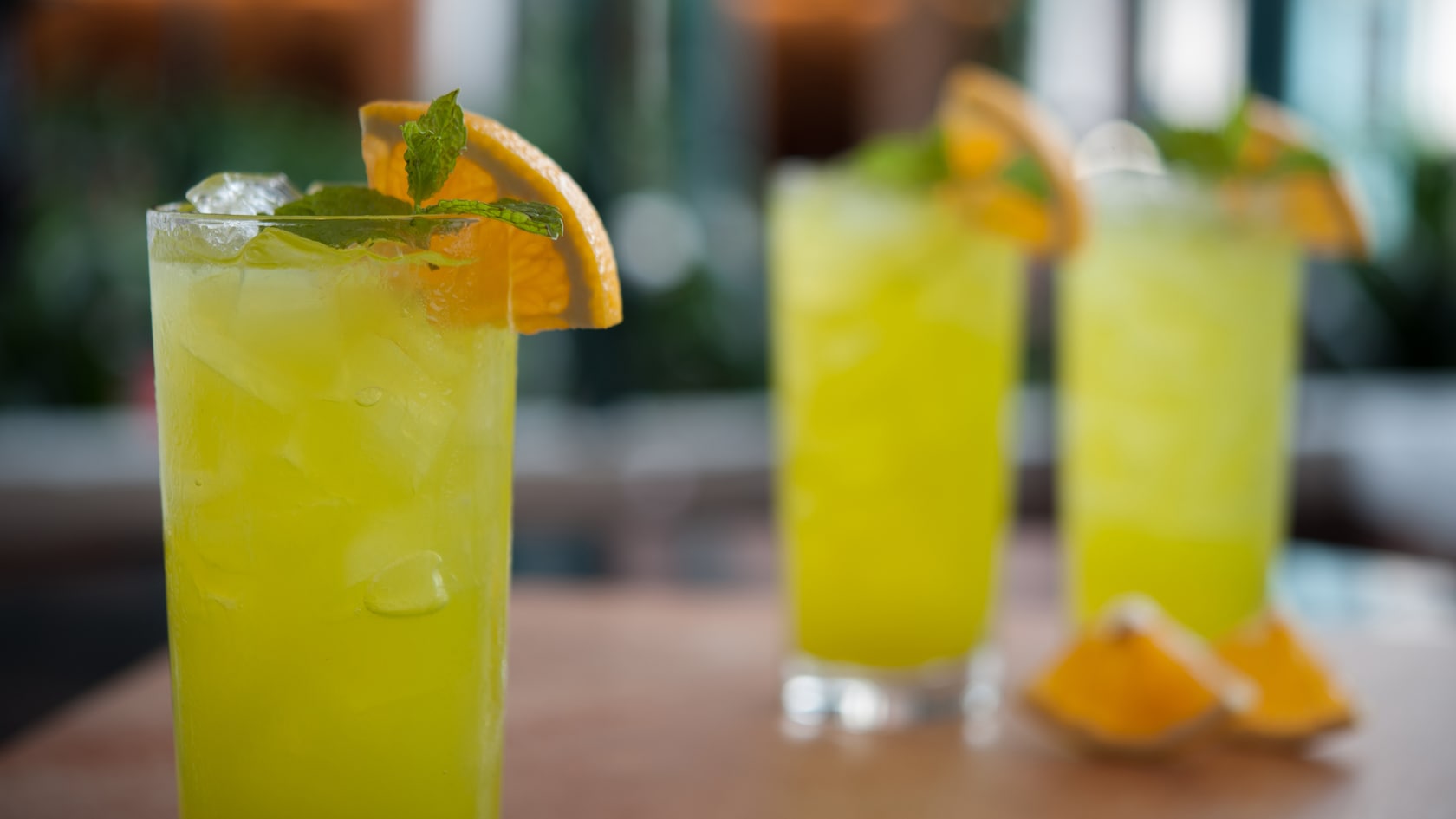Luminescent cocktails prepared with ice in tall glasses and garnished with mint and an orange slice
