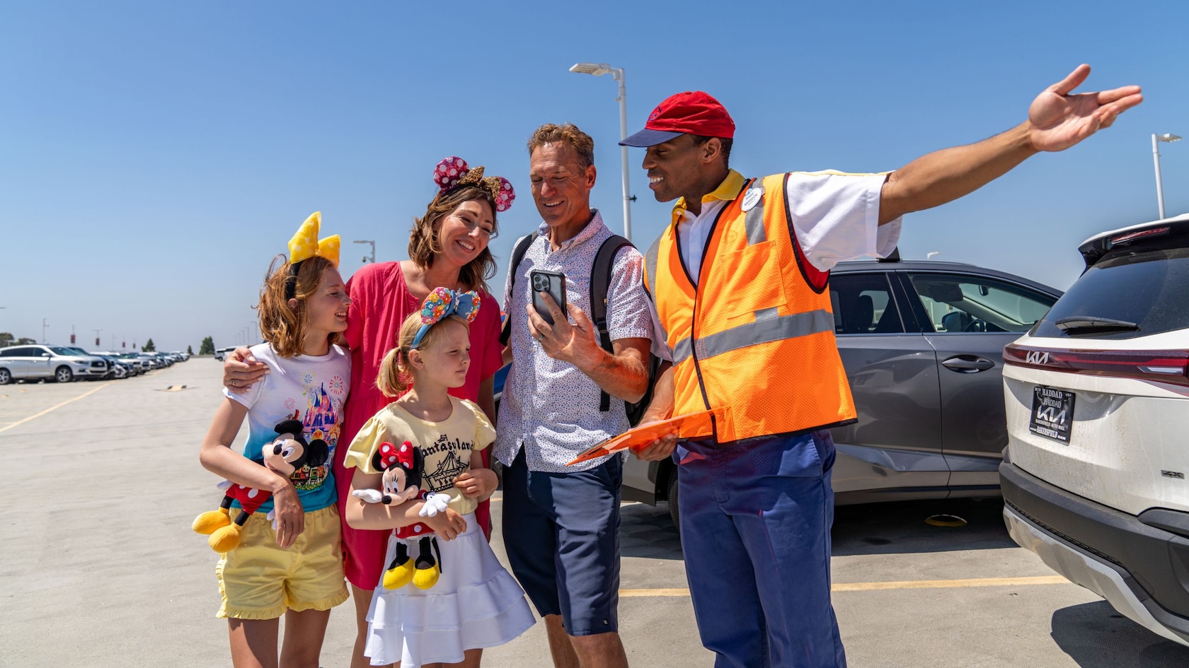 A Disneyland Resort parking cast member in a safety vest points the way for a family in a parking lot