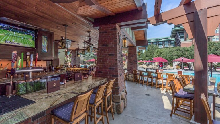 An outside bar with brick pillars and a flat screen television near a pool