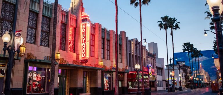 Hollywood Land at dusk, with a neon Hollywood sign on a storefront and palm trees along the street