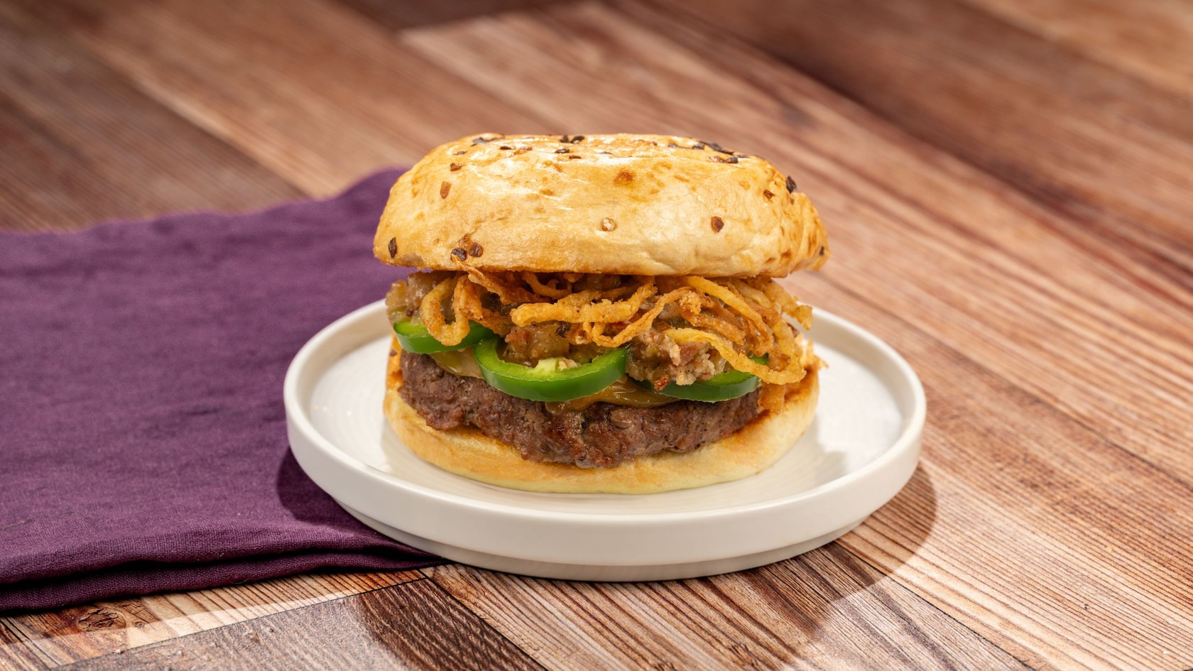 A beef burger with jalapeno cheese sauce, crispy onions and other ingredients on an onion roll