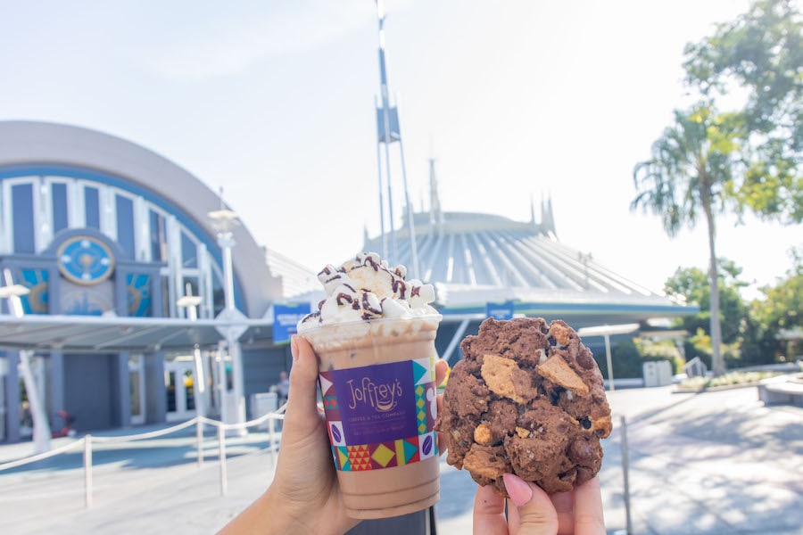 A Joffrey's iced drink topped with whipped cream and a cookie held up in front of Space Mountain at Magic Kingdom