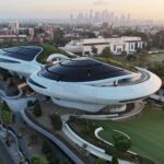 Aerial view of the Lucas Museum of Narrative Art building in Exposition Park, with the downtown Los Angeles skyline behind it