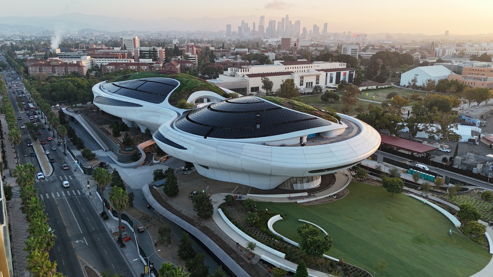 Aerial view of the Lucas Museum of Narrative Art building in Exposition Park, with the downtown Los Angeles skyline behind it