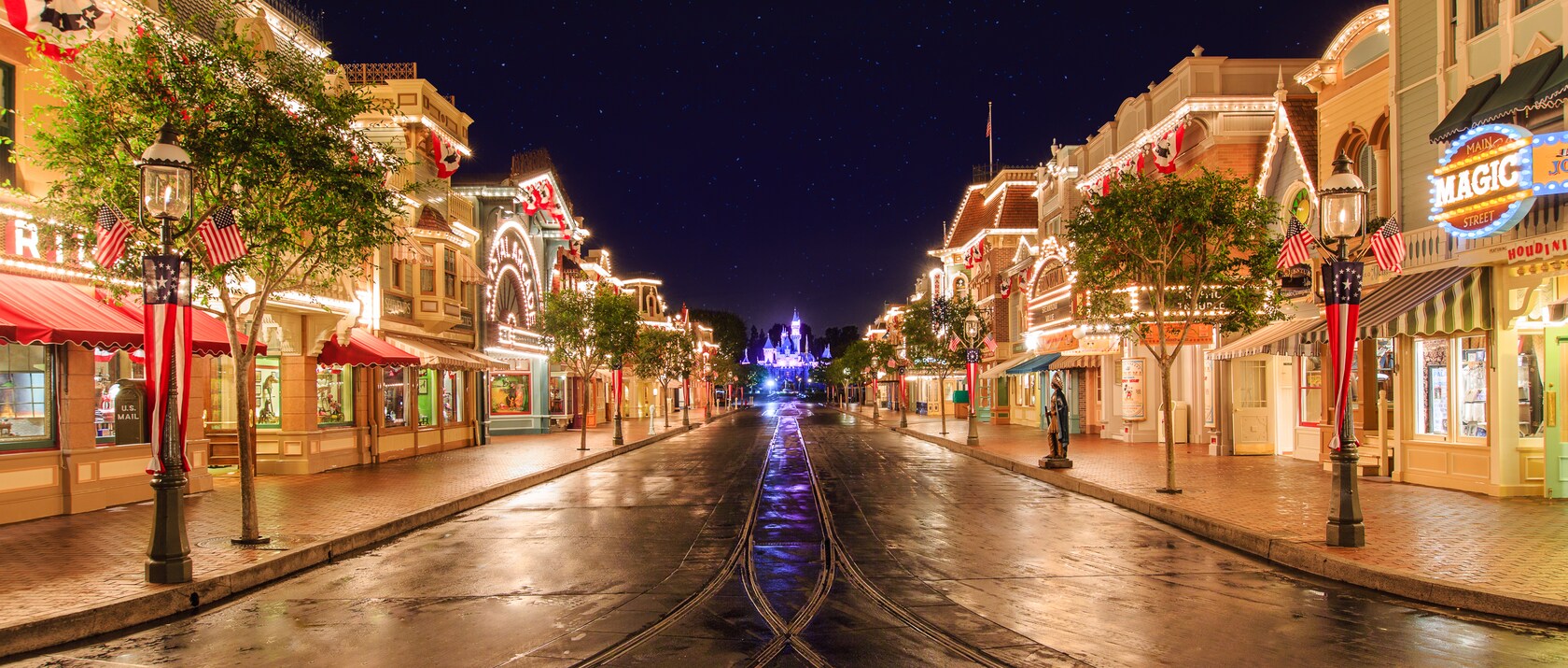 Main Street, U.S.A. at night, with lit storefronts on both sides and the castle glowing at the end of the street