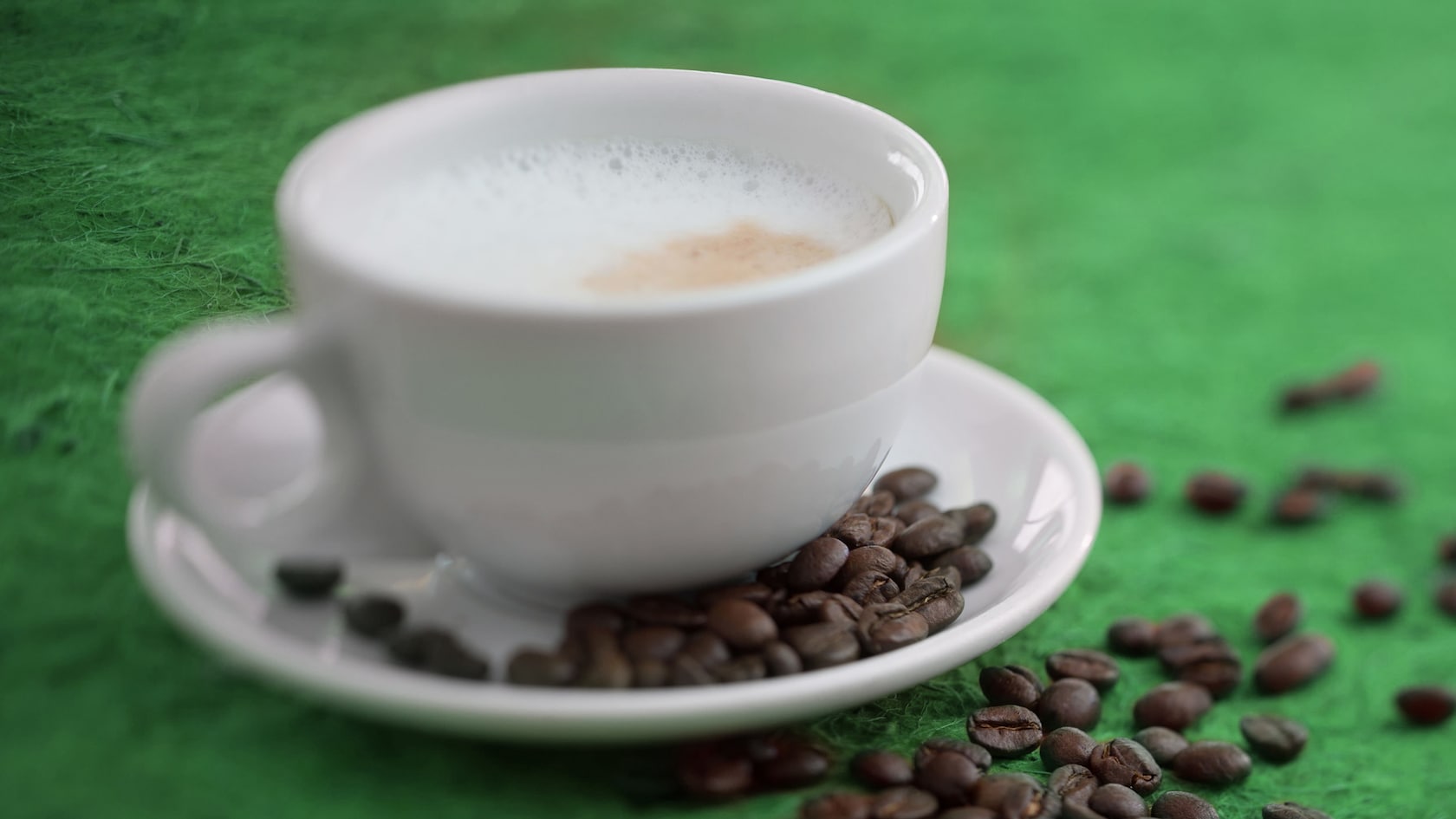 A foamy cup of cappuccino from Starbucks plated beside a scattered array of espresso beans