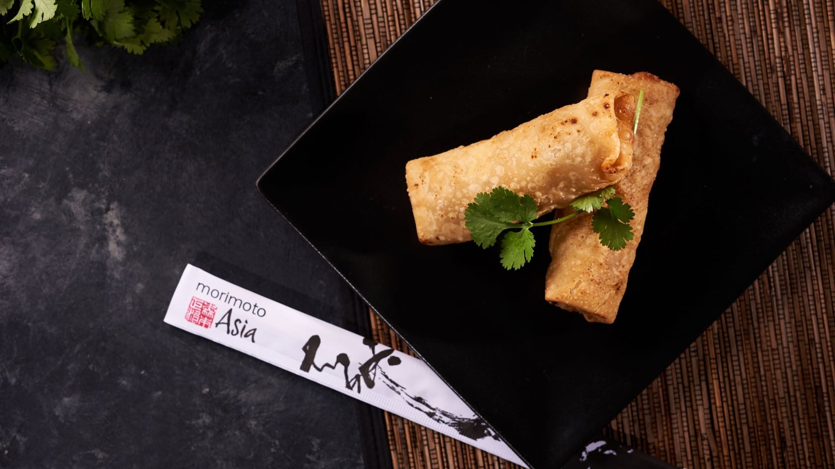 A pair of pork egg rolls and chopsticks displayed on a bamboo placemat