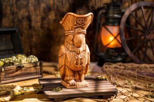 The Pirate Parrot Mug, a sculpted parrot in a tricorn hat with a skull and crossbones, set on a wooden pallet beside a treasure chest and lantern