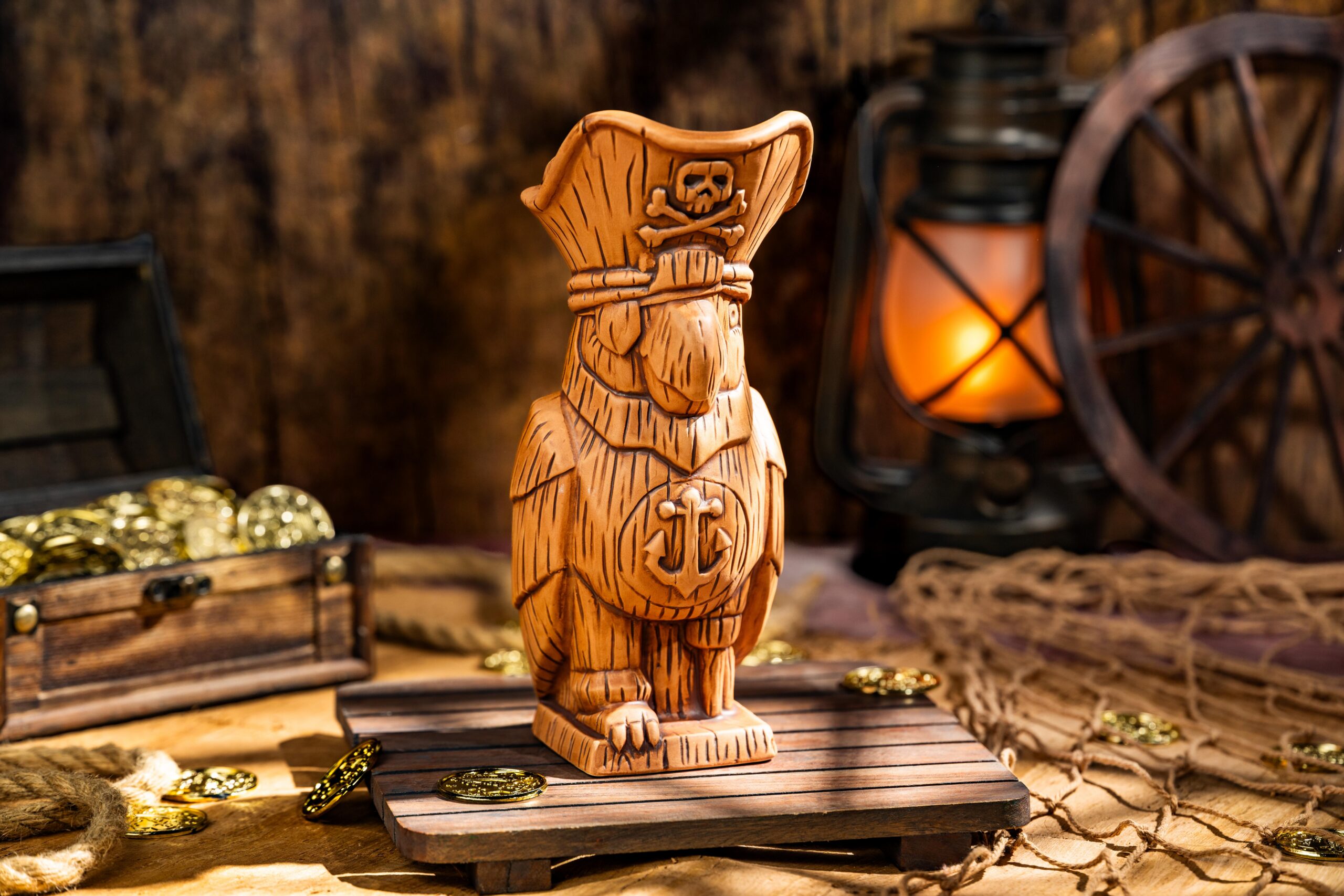 The Pirate Parrot Mug, a sculpted parrot in a tricorn hat with a skull and crossbones, set on a wooden pallet beside a treasure chest and lantern