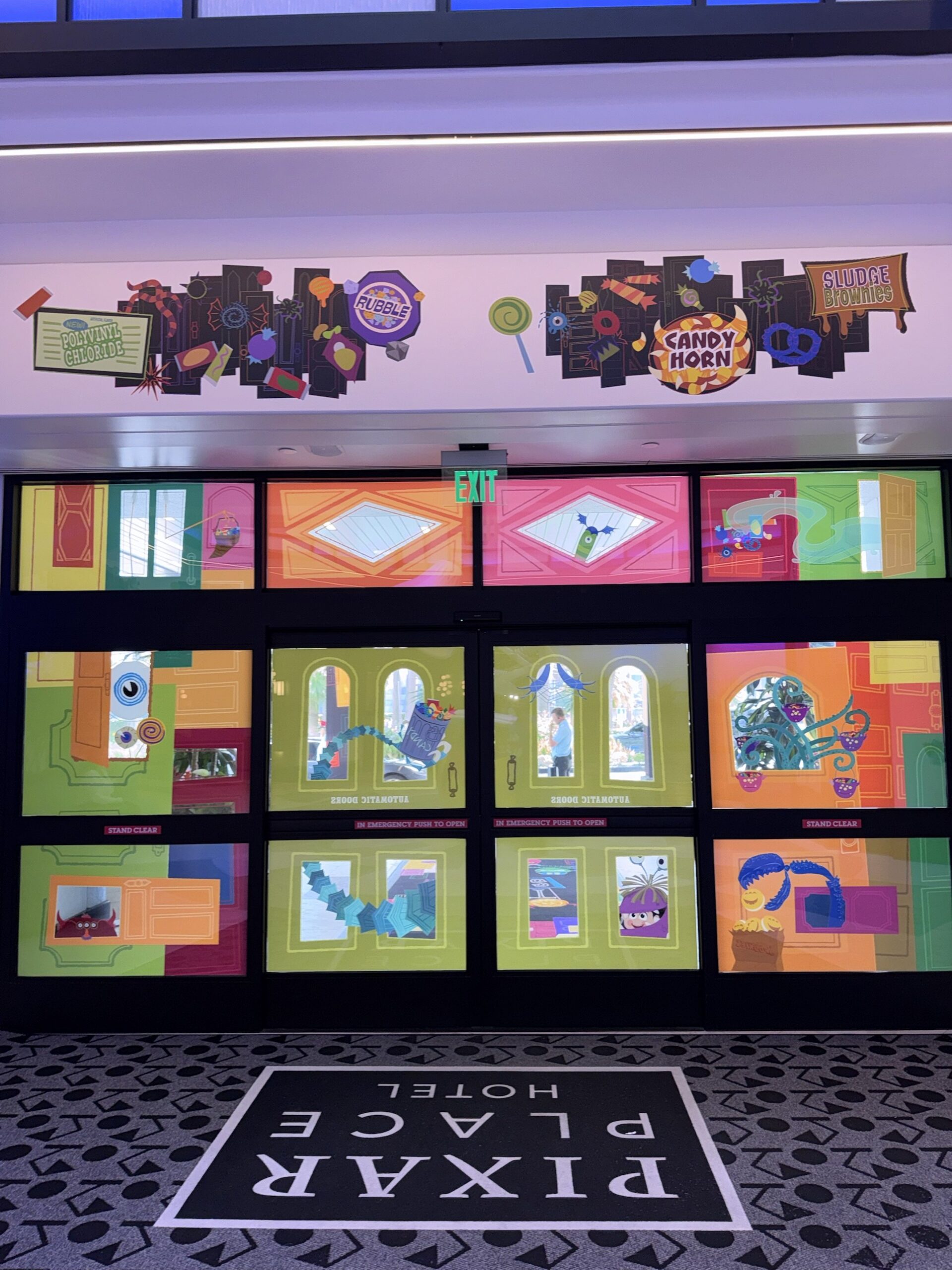 Monster candy wrapper artwork above the Halloween-decorated entrance doors inside Pixar Place Hotel