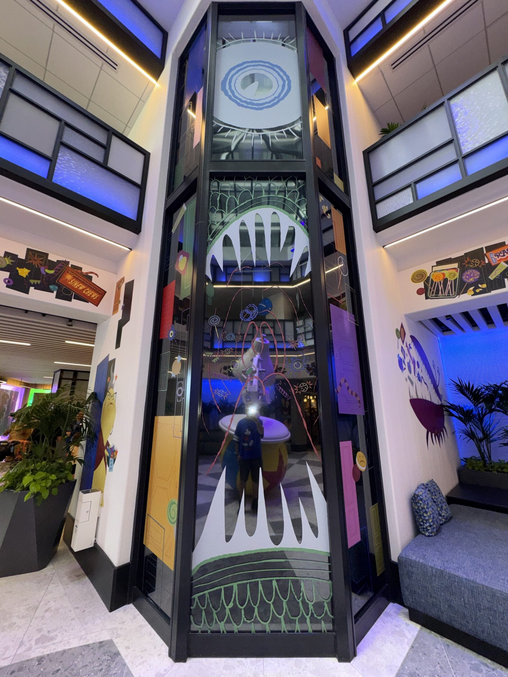 Glass tower in the Pixar Place Hotel lobby decorated with a giant monster eye and a toothy open mouth
