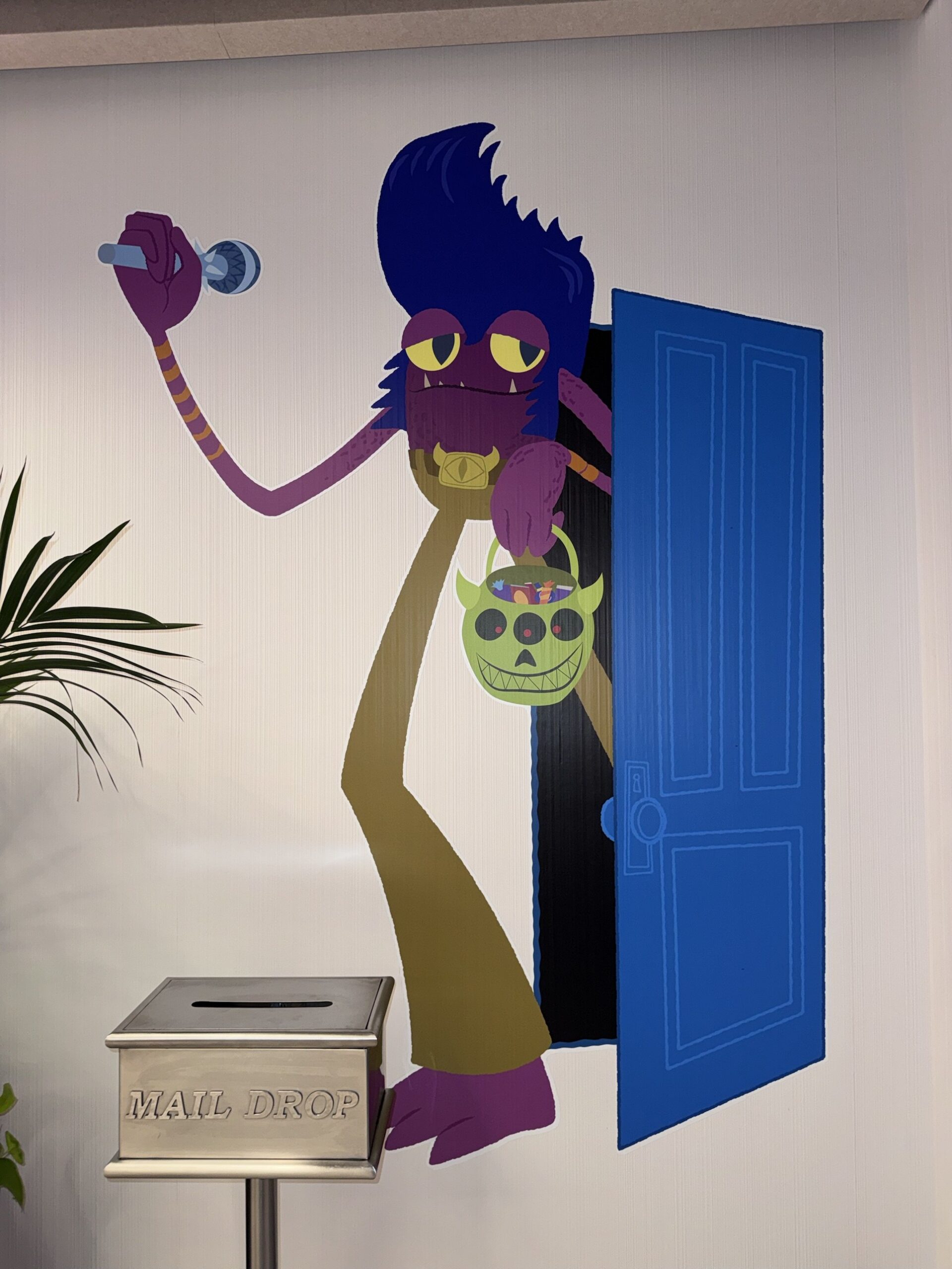 Wall artwork of a purple monster with a pompadour holding a microphone and a trick-or-treat bucket beside a blue door at Pixar Place Hotel