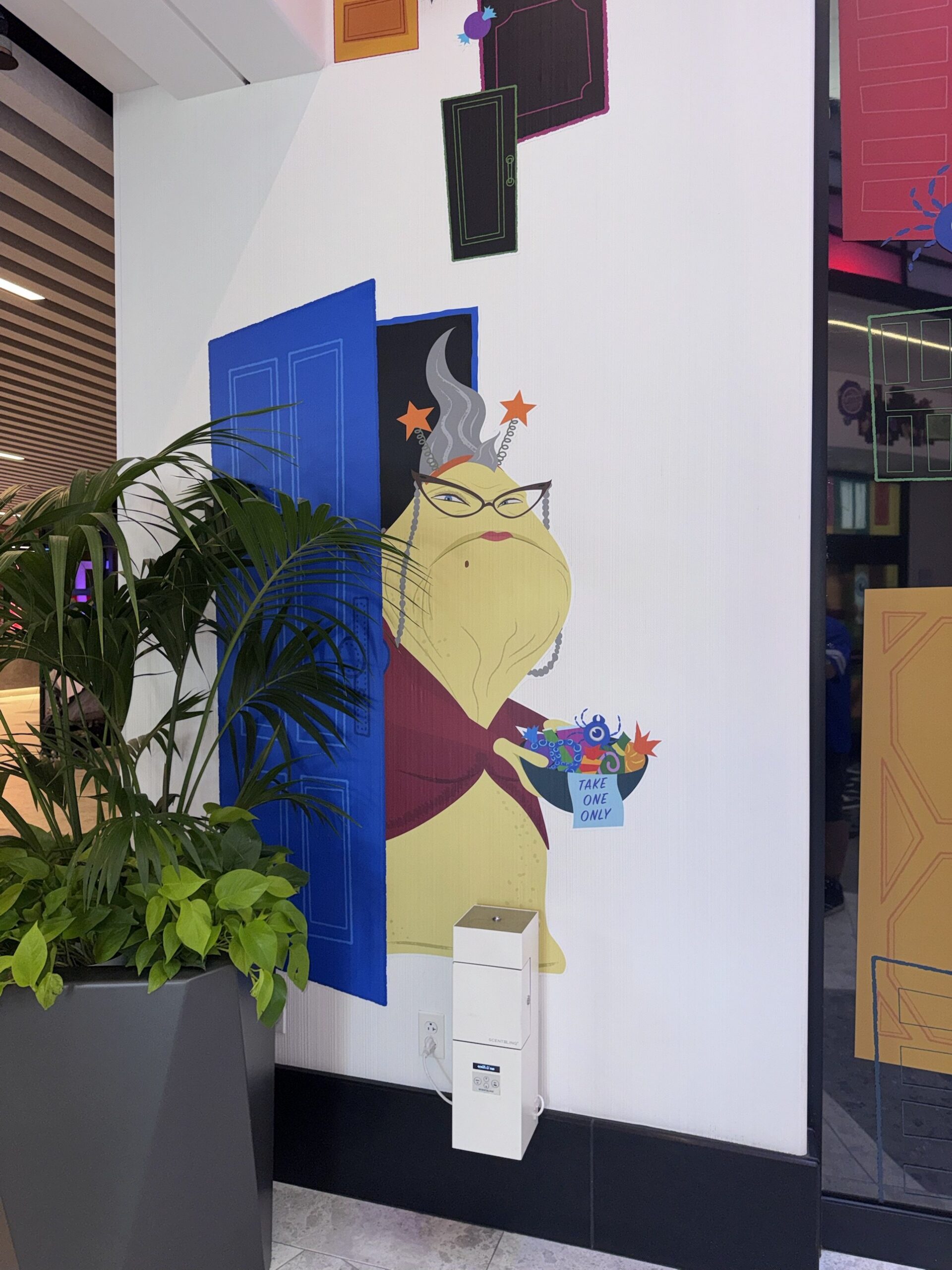 Wall artwork of Roz stepping out of a blue door holding a candy bowl labeled Take One Only at Pixar Place Hotel