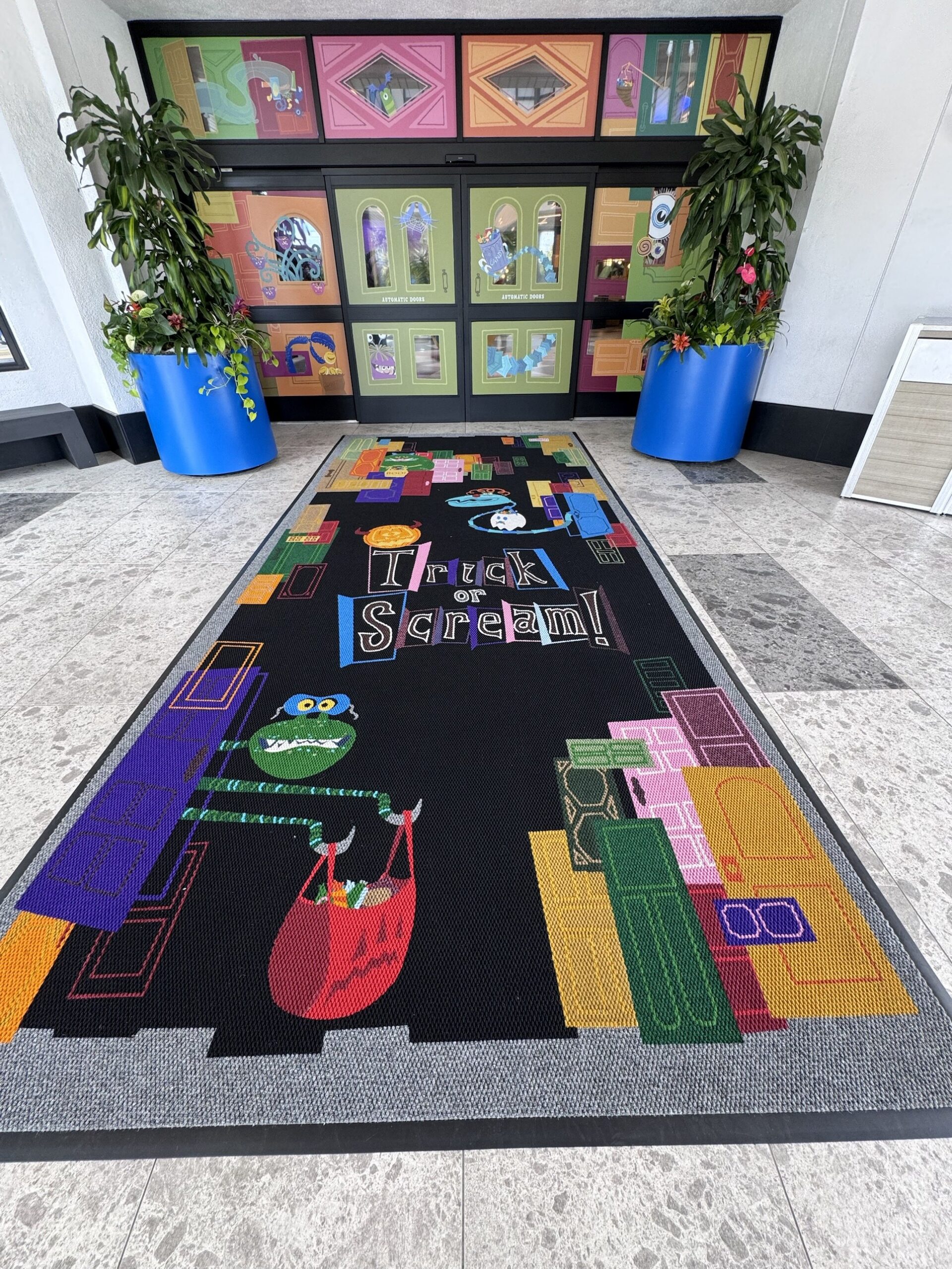 Trick or Scream entry mat with a monster carrying a candy bag in front of Halloween-decorated doors at Pixar Place Hotel