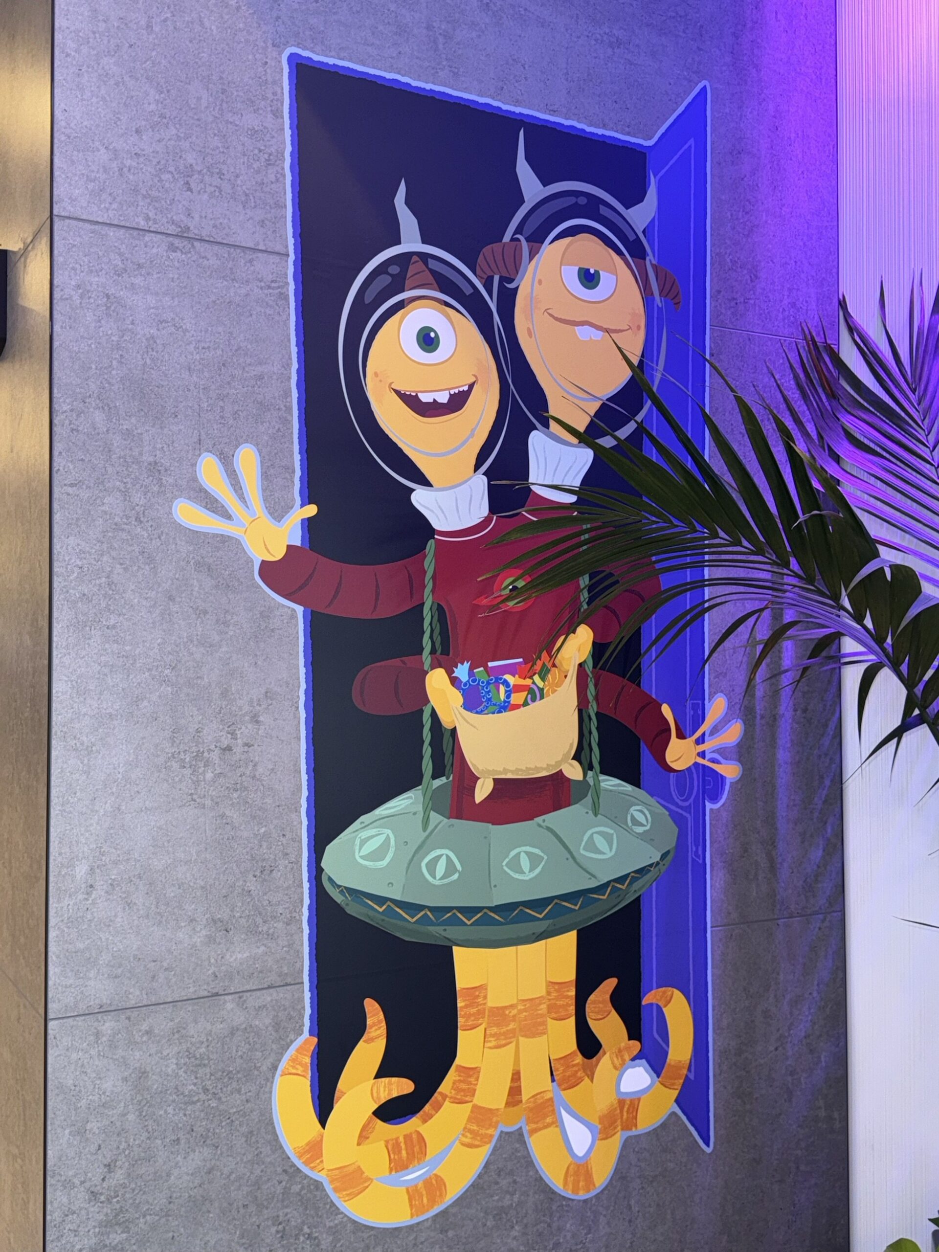 Wall artwork of a two-headed monster in space helmets dressed in a flying saucer costume holding a candy bag at Pixar Place Hotel