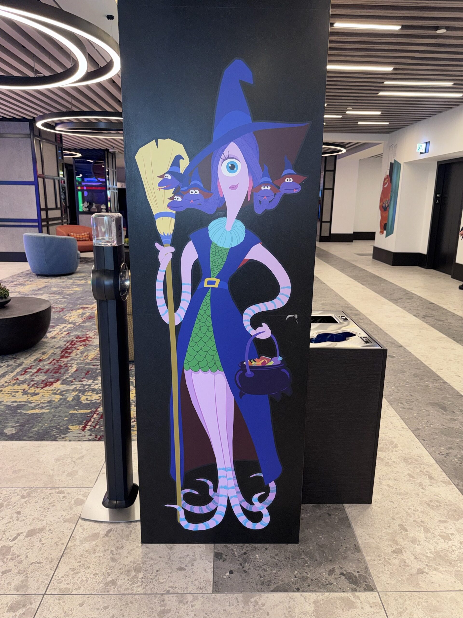 Column artwork of a one-eyed monster dressed as a witch with a broom and cauldron of candy at Pixar Place Hotel