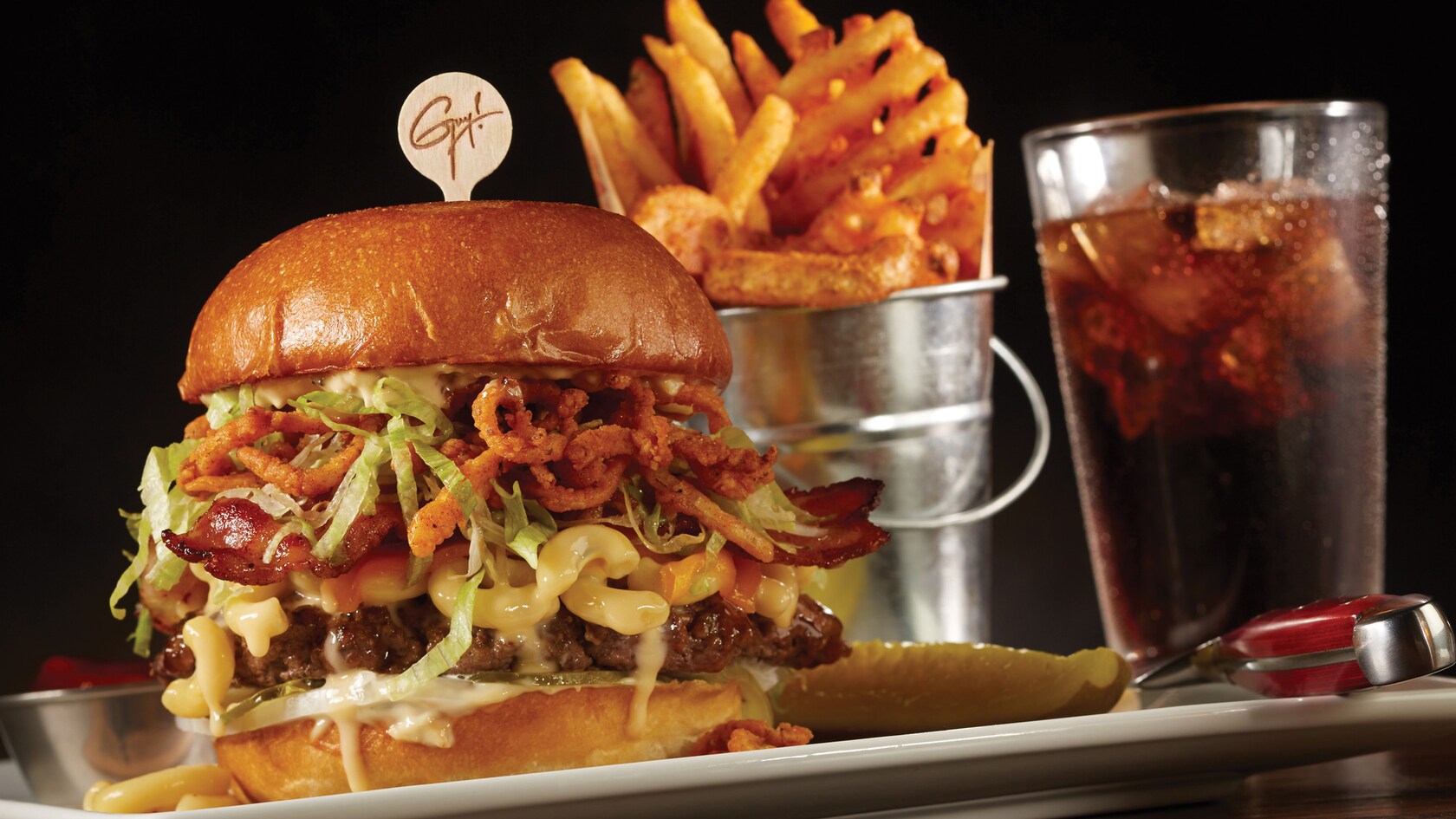 A large burger filled with beef and macaroni & cheese, served with fries and a soda