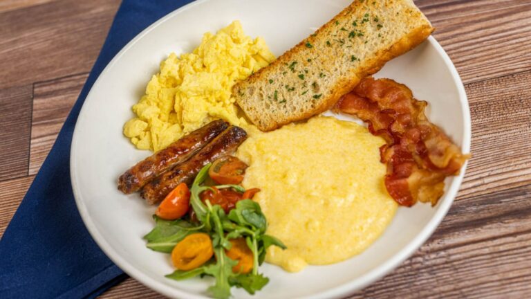 A plate of scrambled eggs, creamy mascarpone polenta, bacon and sausage links from Primo Piatto