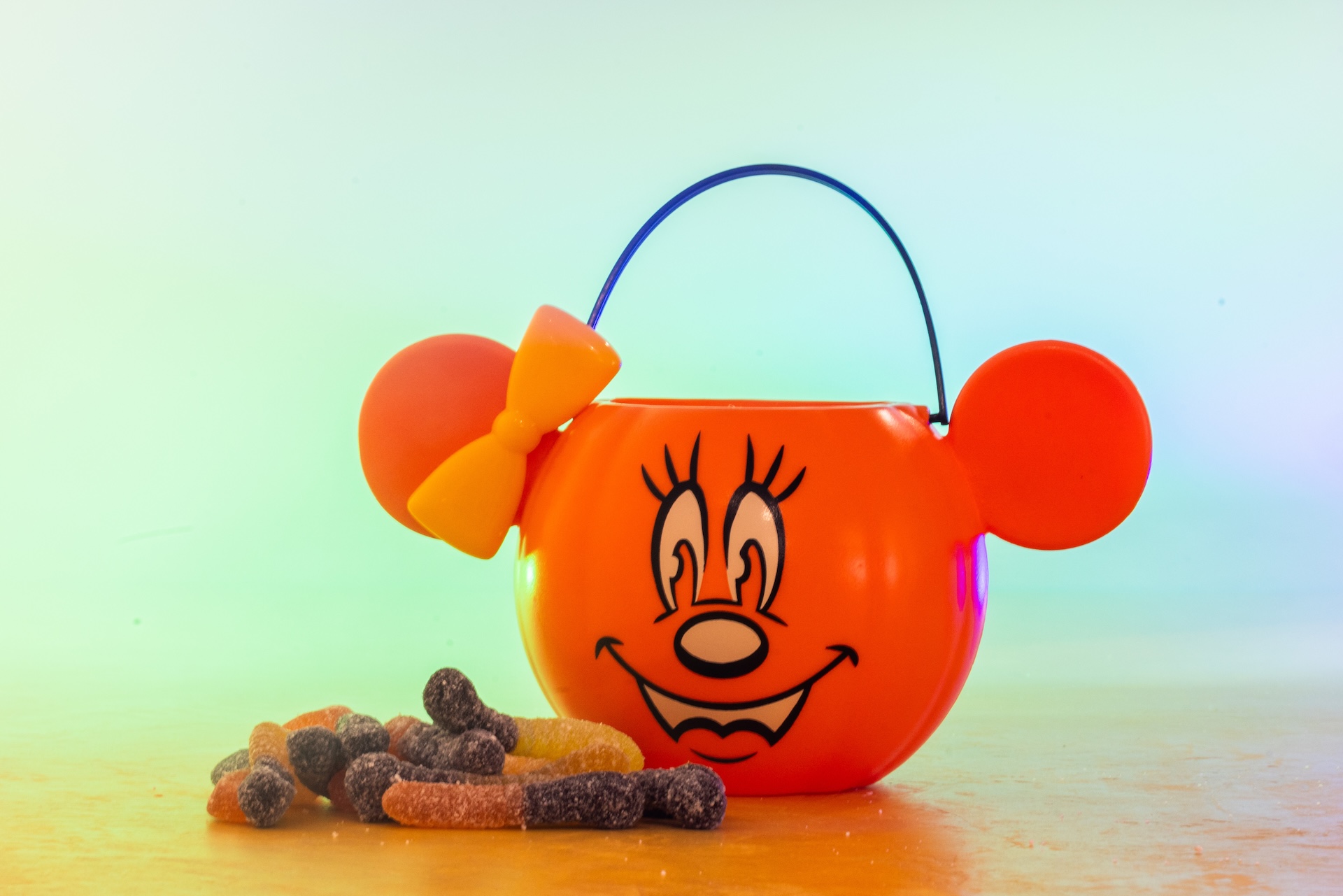 Orange Minnie Mouse pumpkin bucket with a bow, beside a pile of sour gummy worms