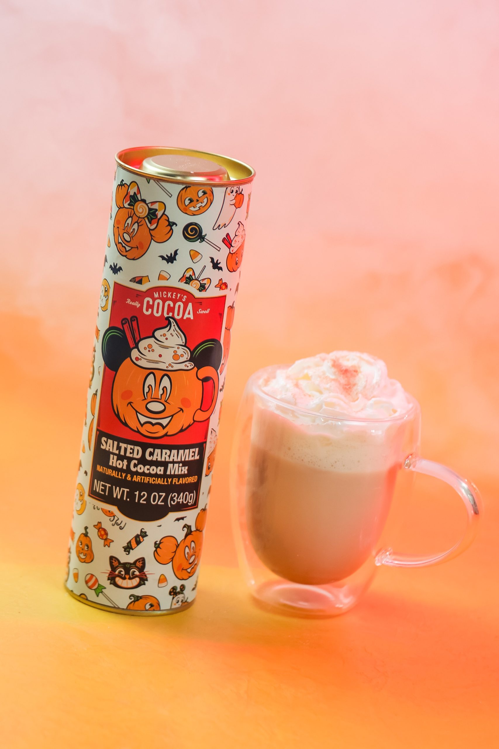 Salted Caramel Hot Cocoa Mix canister with Mickey Mouse pumpkin art beside a glass mug of cocoa