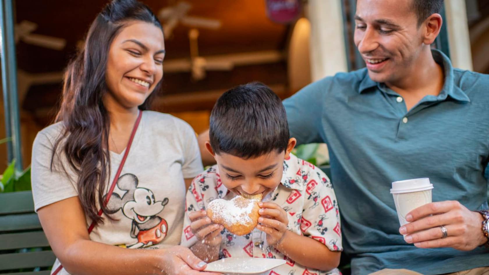 Two parents smile as their kid bites into a beignet