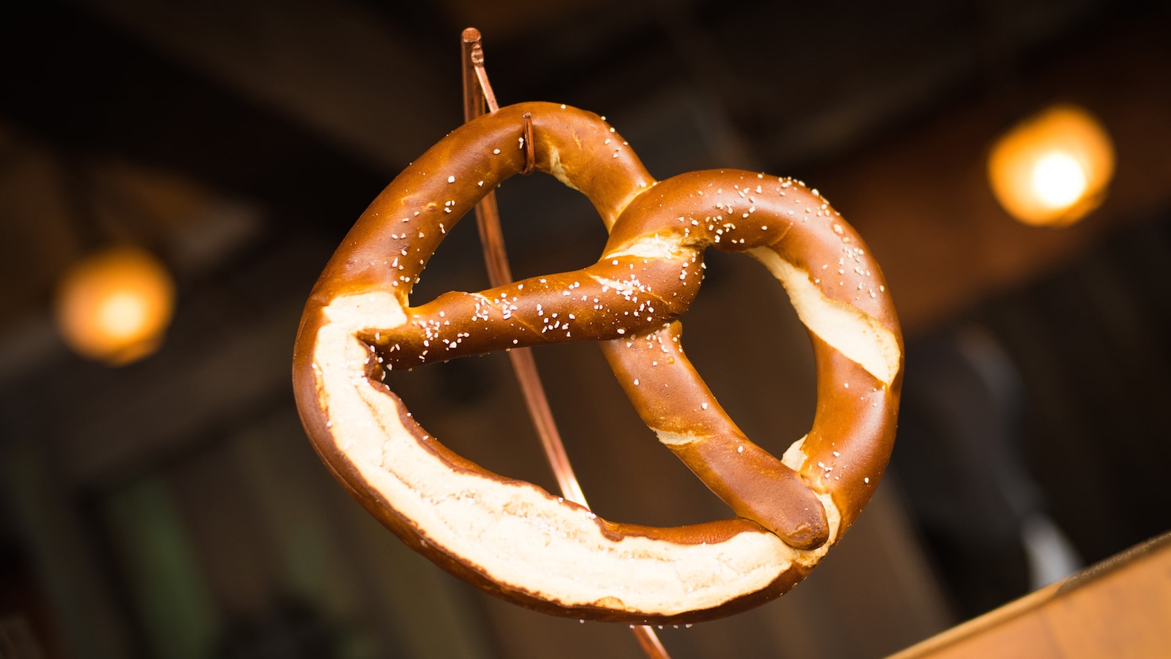 A salted soft pretzel hanging on a display hook