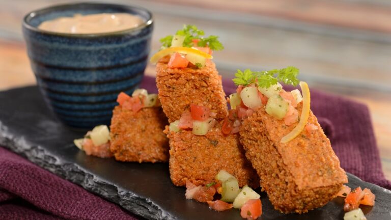 A plate of hummus fries topped with cilantro and chopped vegetables, served with a dipping sauce