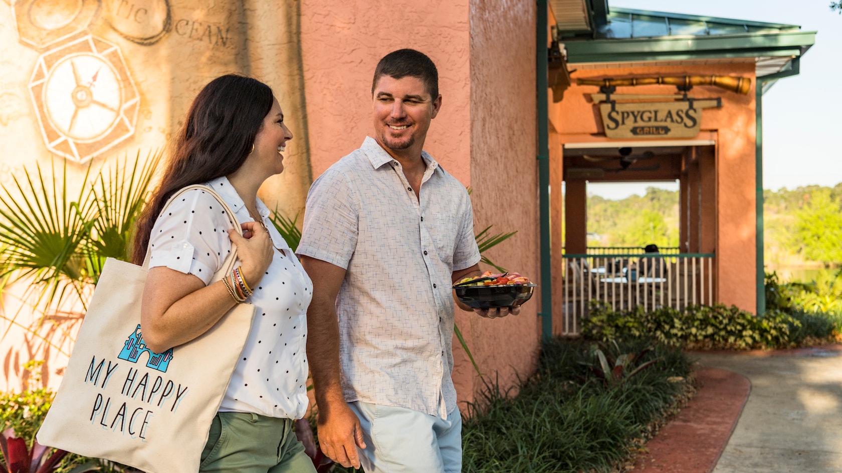 A woman walking next to a man carrying a packaged salad outside a restaurant named Spyglass