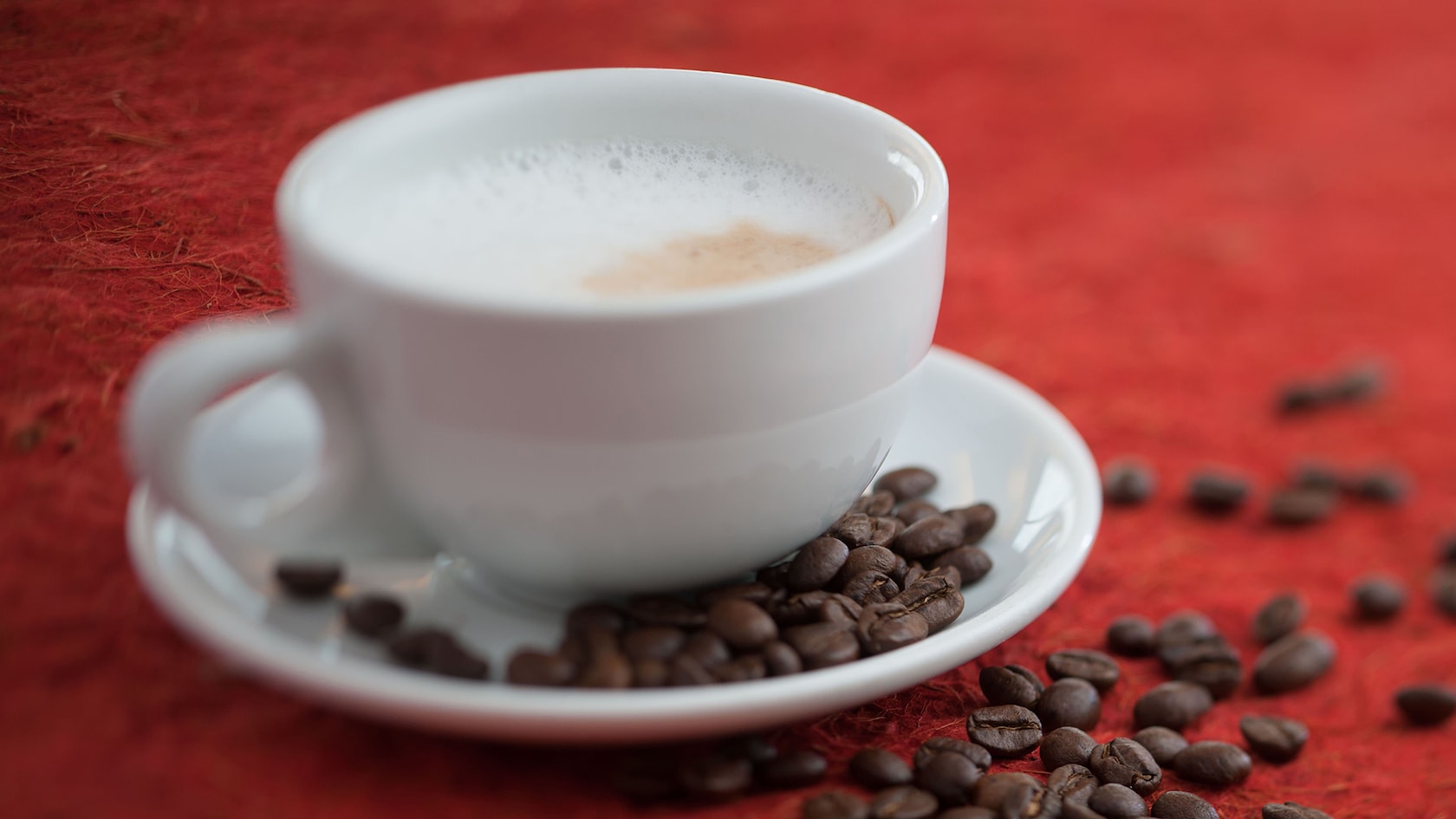 Cup of cappuccino with coffee beans scattered in saucer and on table