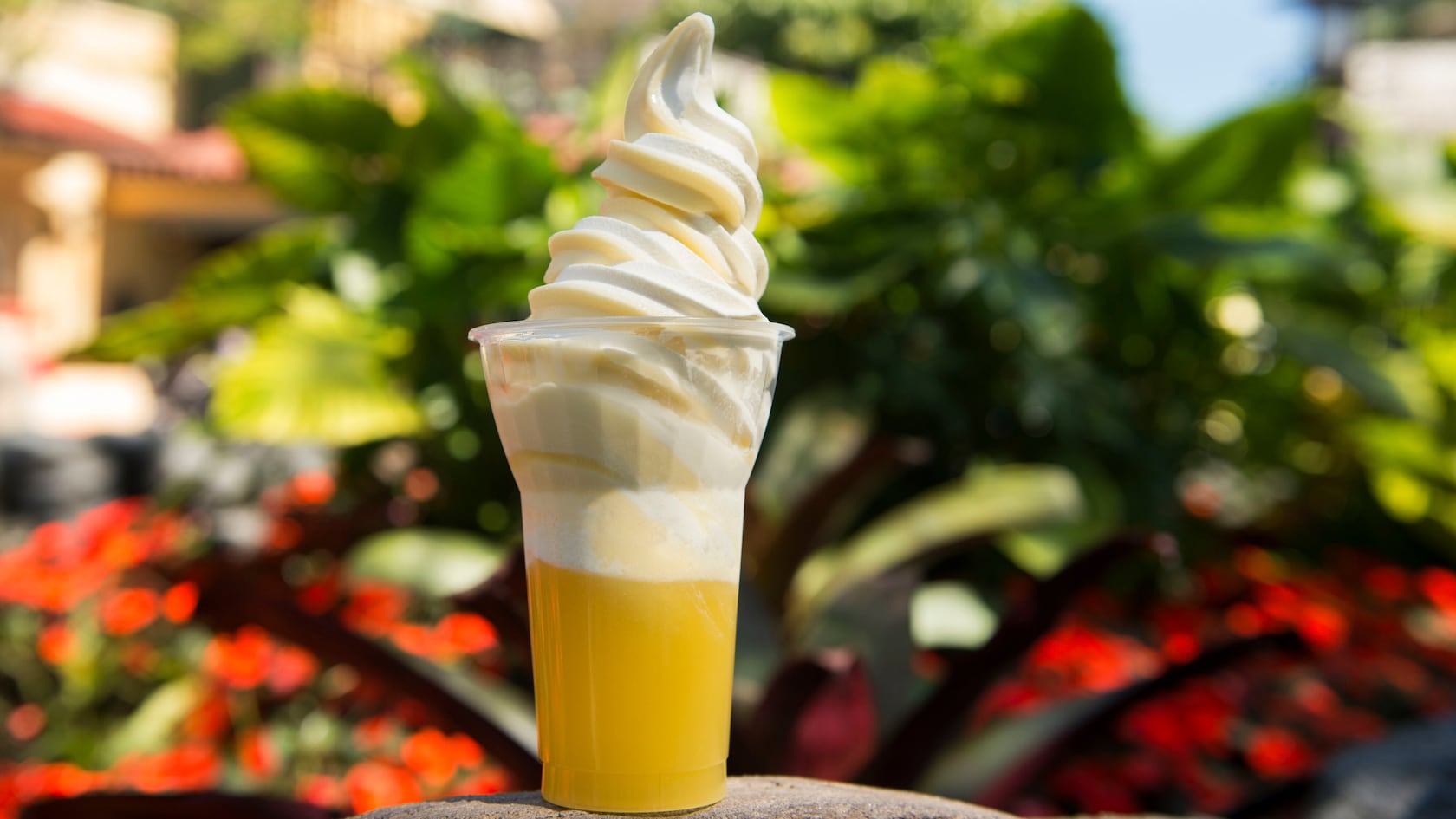 A pineapple Dole Whip, topped with vanilla ice cream with plants in the background