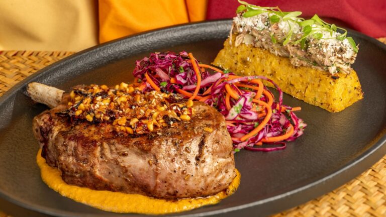 A grilled pork chop with garlic crust on a plate served with cabbage and carrot slaw and corn cake at Tiffins Restaurant