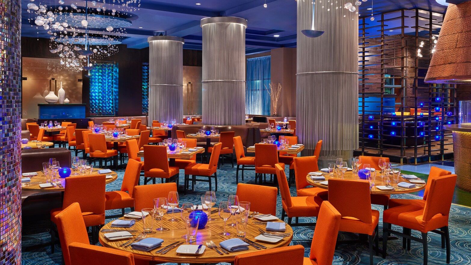A modern restaurant with formally set tables, booths, decorative columns and abstract chandeliers that resemble underwater bubbles