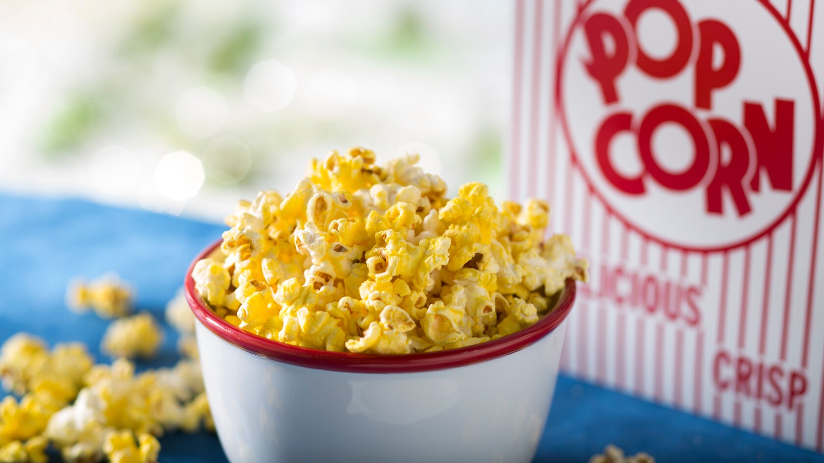 A bowl of buttered popcorn next to a container that reads Popcorn, Delicious, Crisp