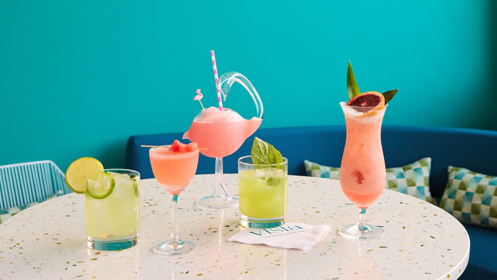 A table set with 5 different drinks next to a wall with a sign that reads ′Vista Parkside Market′