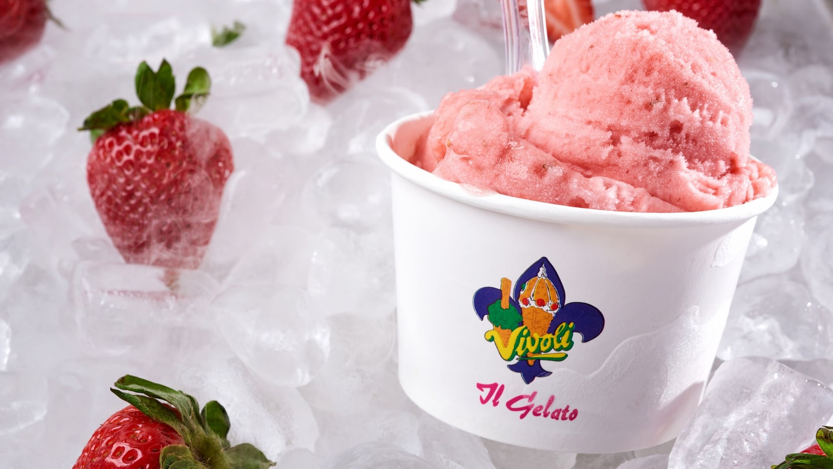 A cup of strawberry frozen dessert on top of ice cubes and surrounded by strawberries