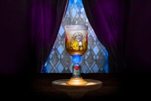 The Be Our Guest Goblet, with a stained-glass style image of Belle and the Beast dancing on the bowl, a lid and straw, a glowing blue section in the stem above a red rose under a clear dome, and a gold base