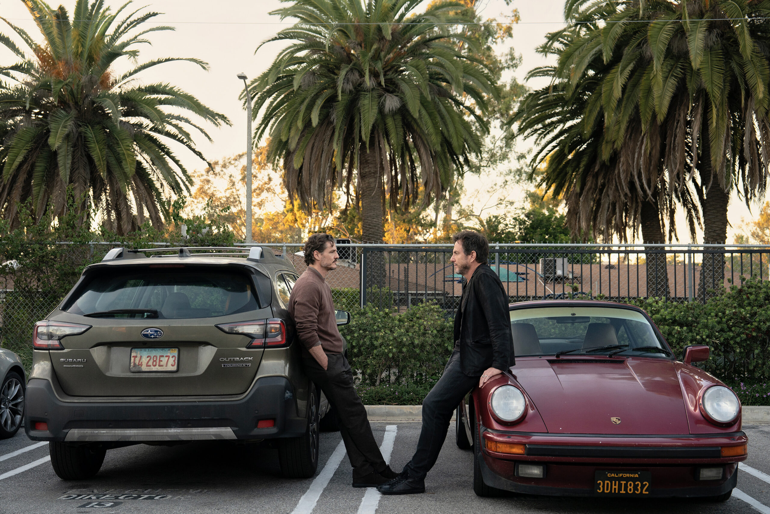 Pedro Pascal and a co-star lean against parked cars under palm trees in a still from Searchlight Pictures' Behemoth!